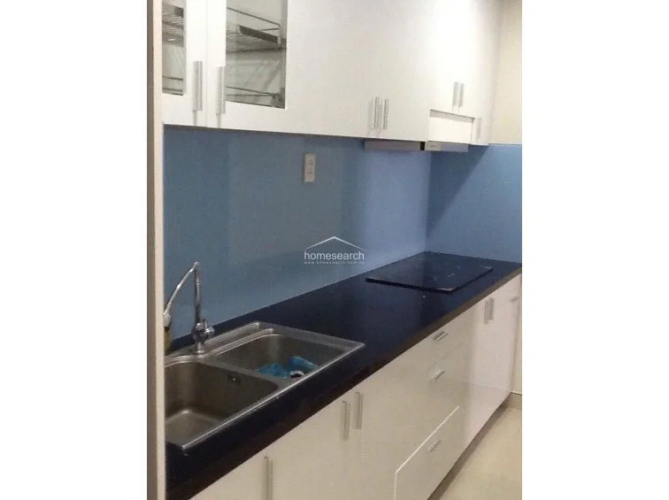 This modern kitchen is characterized by a sleek, linear layout featuring high-gloss white cabinetry, a contrasting black countertop, and a striking light blue glass backsplash. The space is well-equipped with an integrated induction cooktop and a stainless steel double sink, presenting a clean and contemporary design.