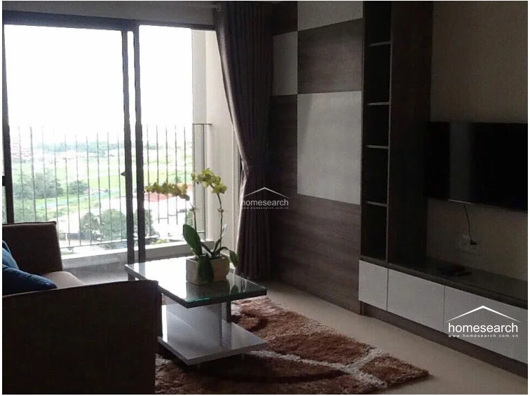 This living area features a modern, neutral color palette with a striking wood-paneled accent wall that incorporates built-in shelving and a TV mount. Large floor-to-ceiling sliding glass doors provide excellent natural light and direct access to a private balcony with an expansive urban view. The space is finished with sleek, light-colored flooring and is maintained in excellent, contemporary condition.