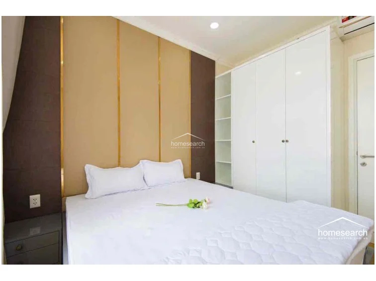 The bedroom is designed with a contemporary aesthetic, featuring a custom headboard with gold trim and dark wood paneling. It includes a built-in white wardrobe with open shelving for display, maximizing storage efficiency while maintaining a minimalist and uncluttered look.
