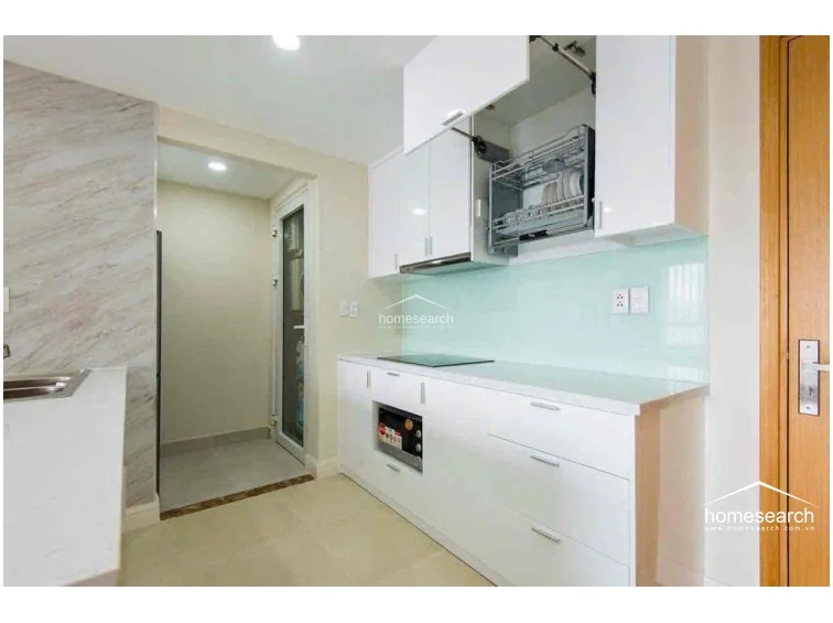 This modern kitchen features white cabinetry with integrated storage solutions, including a convenient pull-down dish rack, and a light-colored glass backsplash. The space is finished with light tile flooring and marble-patterned wall accents, offering a clean, organized, and well-maintained cooking environment.