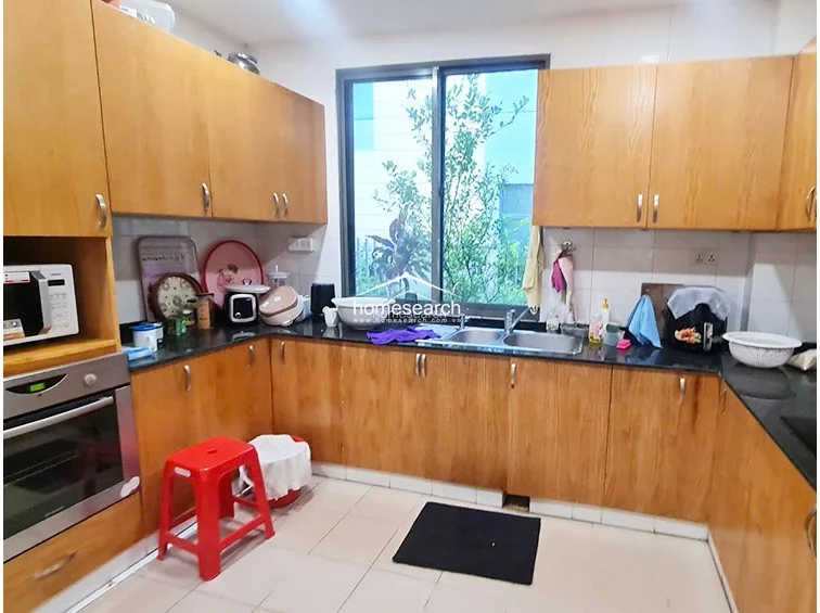 This U-shaped kitchen features warm-toned wooden cabinetry with ample storage and a contrasting black granite countertop. It includes a built-in oven and a central window that provides natural light and a view of the greenery outside, while the floor is finished with neutral-colored tiles.