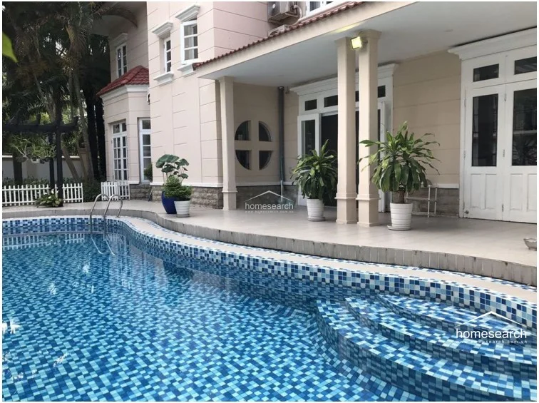 This image highlights a private swimming pool with a mosaic tile finish, directly accessible from the villa's covered terrace. The outdoor space is furnished with potted plants and features a clean, neutral-toned patio area, creating an ideal environment for relaxation and outdoor entertaining.