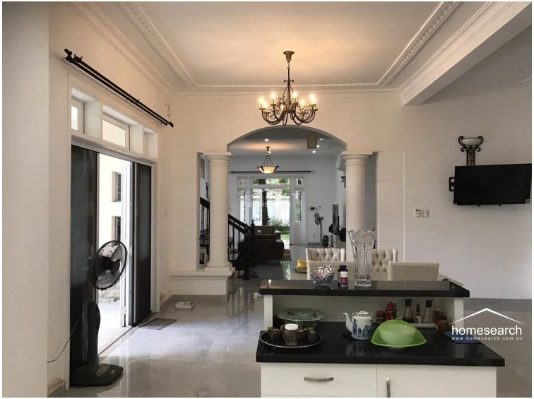This view from the kitchen area looks toward the living room, emphasizing the home's airy, interconnected flow and high ceilings with decorative crown molding. The kitchen is equipped with a functional island featuring a black countertop, while a classic chandelier adds a touch of elegance to the dining and transition spaces.