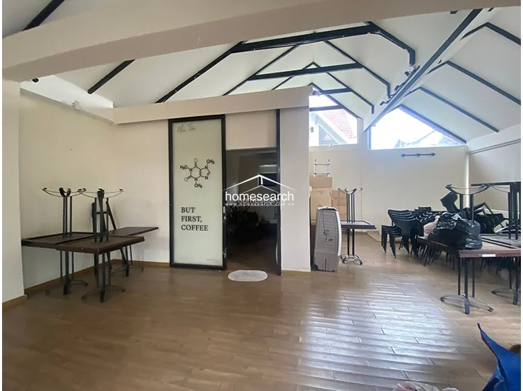 This area appears to be a commercial or dining space, highlighted by a glass door featuring a coffee-themed graphic. The room maintains the high, vaulted ceiling design and wood-look flooring, offering a flexible layout that is currently used for storage and seating.