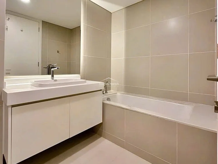 The bathroom is finished in neutral, large-format beige wall tiles and features a clean, white vanity with a modern basin and a large mirror. It includes a deep soaking tub with integrated fixtures, reflecting a well-maintained, high-quality condition consistent with a modern residential build.