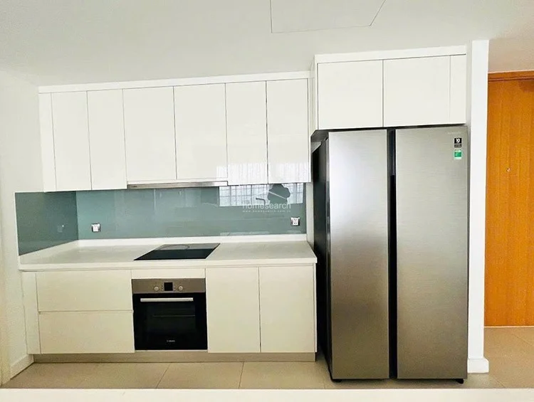 The kitchen is equipped with high-quality stainless steel appliances, including a built-in oven and a full-size side-by-side refrigerator. It features clean white cabinetry, a light-colored countertop, and a sleek, pale blue glass backsplash that adds a subtle pop of color. The layout is compact yet highly functional, maintaining the property's overall standard of modern, high-end design.