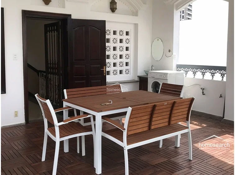 This rooftop terrace features durable wood-look decking and a functional outdoor dining set, perfect for al fresco meals. The space includes a convenient laundry area with a washing machine and a wall-mounted sink, set against a backdrop of decorative lattice brickwork and white walls.