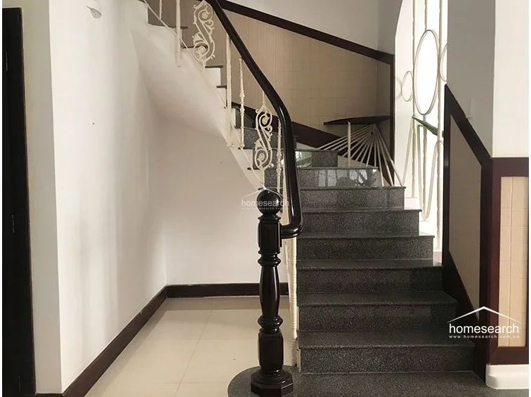 This staircase features elegant dark wood handrails paired with ornate white metal balusters, creating a sophisticated architectural focal point. The steps are finished in polished dark granite, and the surrounding walls are kept in a clean, minimalist white finish.