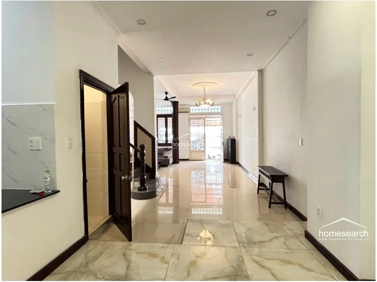 This view from the kitchen looking toward the front entrance highlights the home's deep, open floor plan and consistent marble-style flooring. The space connects the kitchen, a ground-floor bathroom, and the living area, featuring a classic chandelier and decorative crown molding.