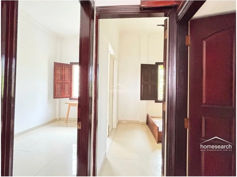 This view from the hallway highlights the flow between two adjacent bedrooms, both featuring consistent dark wood doors and frames. The transition space is clean and bright, showcasing the continuity of the light tile flooring and simple architectural lines throughout the floor.