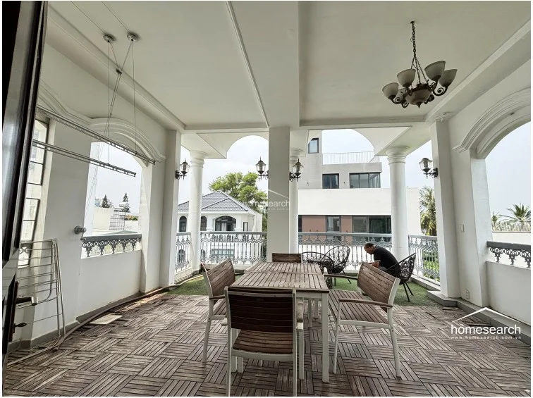 This expansive, covered terrace features an open-air layout with classic architectural columns and arched openings that provide panoramic neighborhood views. The space is finished with wood-look tile flooring, a decorative chandelier, and includes a central dining set, making it an ideal area for outdoor entertaining.