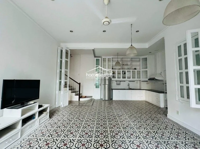 This open-concept living and kitchen area features striking patterned tile flooring and a bright, white color scheme that enhances the sense of space. The kitchen is equipped with extensive white cabinetry, a stainless steel refrigerator, and a sleek countertop, while the room is illuminated by a mix of pendant lighting, recessed lights, and a ceiling fan.