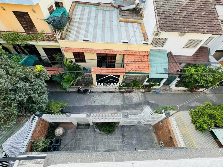 This aerial perspective provides an overview of the property's exterior, including a gated courtyard with paved flooring and surrounding greenery. The neighborhood consists of multi-story residential buildings with a mix of tiled roofs and balconies, reflecting a dense urban setting. The property appears well-defined with secure perimeter walls and a clear, functional outdoor footprint.
