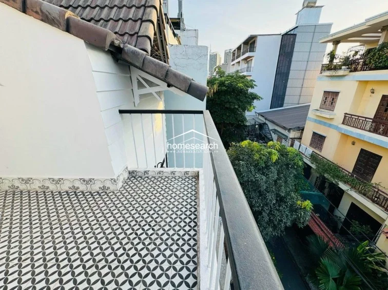 This outdoor balcony features decorative patterned floor tiles and a minimalist white railing, offering an elevated view of the surrounding neighborhood and greenery. The space is well-maintained and connects seamlessly to the interior, providing a private spot for fresh air and relaxation.