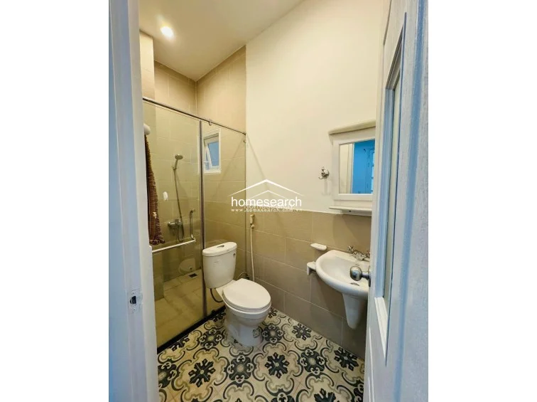 This bathroom features a functional layout with a glass-enclosed shower area and a pedestal sink. The space is finished with neutral wall tiling and decorative patterned floor tiles, creating a clean and well-maintained appearance.