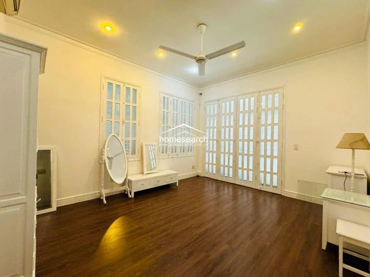 This bright bedroom is finished with warm wood flooring and white walls, creating an airy and inviting living space. It includes a ceiling fan, recessed lighting, and elegant French-style louvered doors that provide access to the rest of the home.