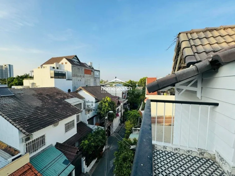 This outdoor balcony offers an elevated view of the surrounding neighborhood and leafy streetscape. The space is finished with decorative patterned tiles and features a simple metal railing, providing a pleasant area for fresh air.
