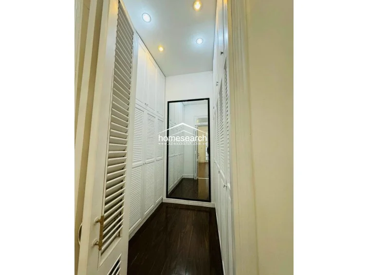 This dedicated walk-in closet space is lined with floor-to-ceiling white louvered cabinetry, offering extensive storage capacity. The room is finished with dark wood flooring and a large full-length mirror, creating a polished and functional dressing area.