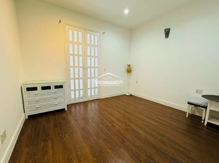 This bedroom features warm wood-tone flooring and crisp white walls, creating a clean and neutral aesthetic. A set of white French doors provides natural light and access to an outdoor area, while a white chest of drawers offers functional storage.