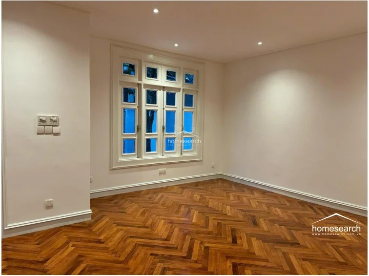 This interior room showcases elegant herringbone-patterned wooden flooring and crisp white walls, creating a bright and sophisticated atmosphere. A large, multi-pane window allows for ample natural light, while recessed ceiling lights provide clean, modern illumination.