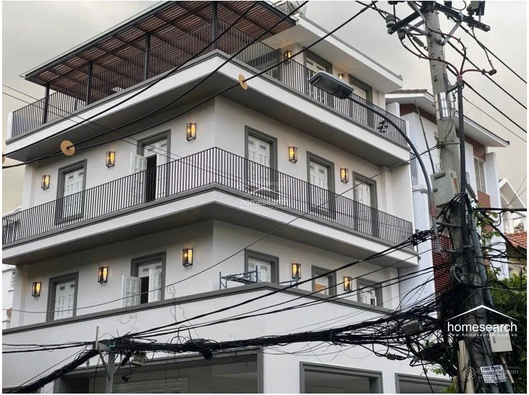 This view captures the exterior of a multi-level residential building with a contemporary design, featuring wrap-around balconies on each floor and a covered rooftop terrace. The building is finished in a neutral color palette with black metal railings and exterior wall sconces, showcasing a modern and well-maintained architectural style.