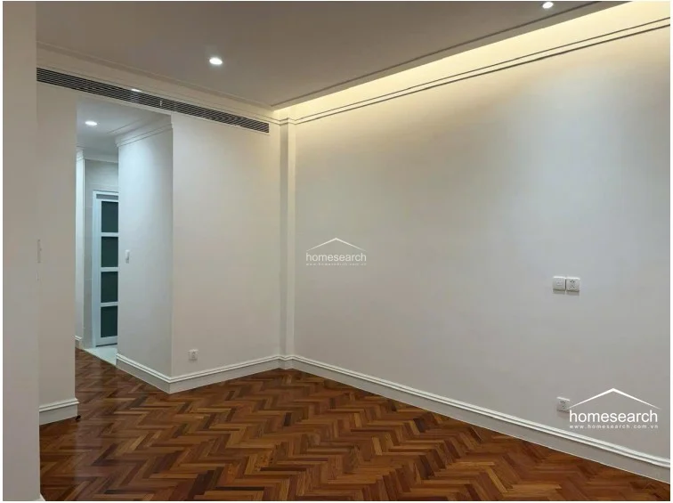 This view highlights an interior hallway or transition space that maintains the consistent design language of the home, including herringbone wood flooring and clean white walls. A recessed ceiling vent suggests the presence of a central air conditioning system, ensuring climate control throughout the property. The space leads into another room, showcasing an open and connected layout with modern, minimalist aesthetics.