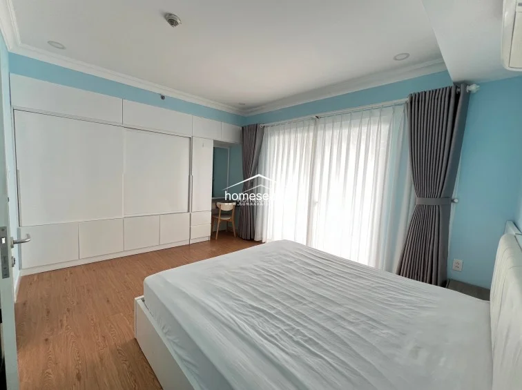 This bedroom layout emphasizes storage efficiency with a large, wall-to-wall white wardrobe unit that seamlessly integrates a vanity area. The room is finished with light blue paint and wood-look flooring, maintaining a consistent and cohesive design throughout the space.