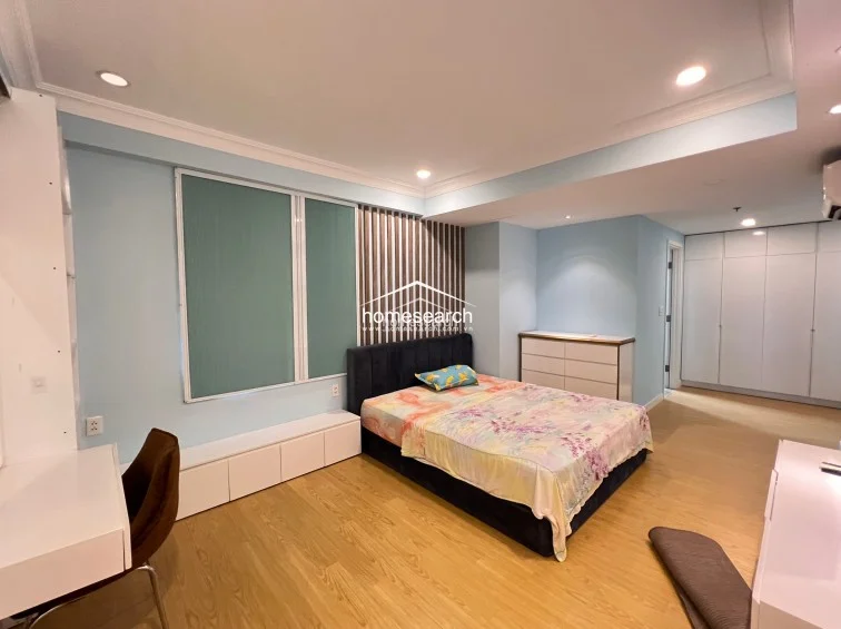 This view highlights the bedroom's functional layout, featuring a dedicated workspace with a desk and chair alongside a low-profile storage bench under the windows. The expansive wall of white cabinetry provides generous storage, while the recessed lighting and clean lines contribute to a bright, well-organized living environment.
