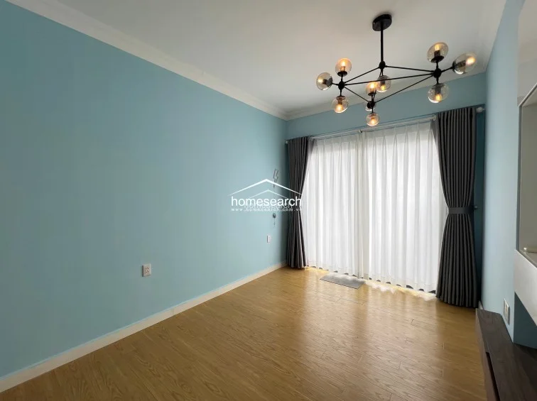 This bedroom is defined by a striking, modern multi-bulb chandelier and floor-to-ceiling curtains that provide soft natural light. The space is finished with light blue walls and wood-look flooring, offering a clean and minimalist aesthetic.