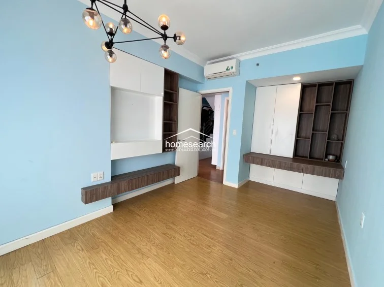 This room is highly functional, featuring extensive built-in cabinetry and shelving units in a two-tone white and wood finish. It is equipped with a wall-mounted AC unit and maintains a consistent design language with light blue walls and wood-look flooring.