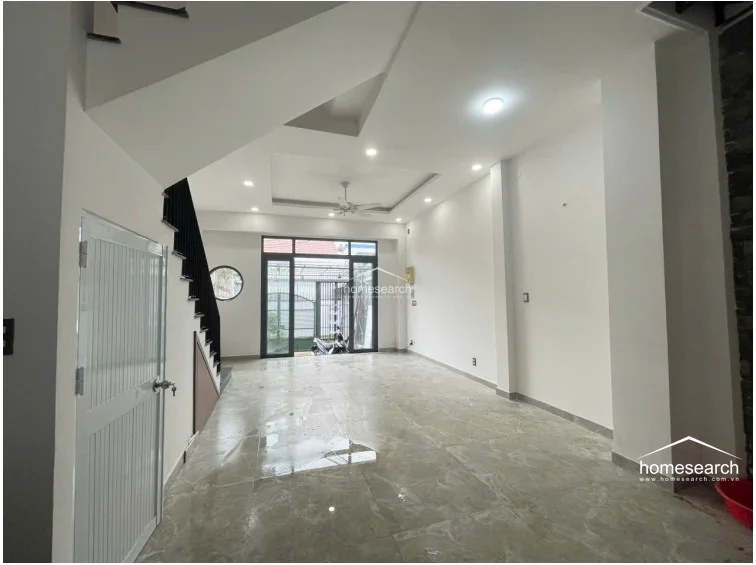 This view from the rear of the living room looking toward the entrance emphasizes the depth of the floor plan and the natural light provided by the large glass front doors. The inclusion of a unique circular window adds an architectural point of interest to the otherwise clean, white-walled interior.