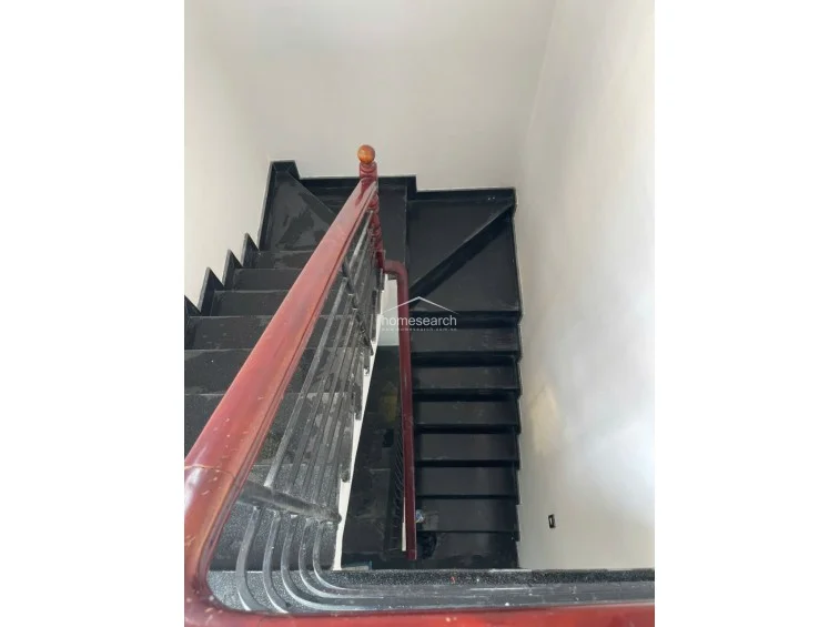 The interior staircase is finished with dark, high-gloss stone steps that contrast sharply against the minimalist white walls. A sturdy, polished wooden handrail paired with a simple metal balustrade provides a classic, clean architectural detail for vertical circulation.
