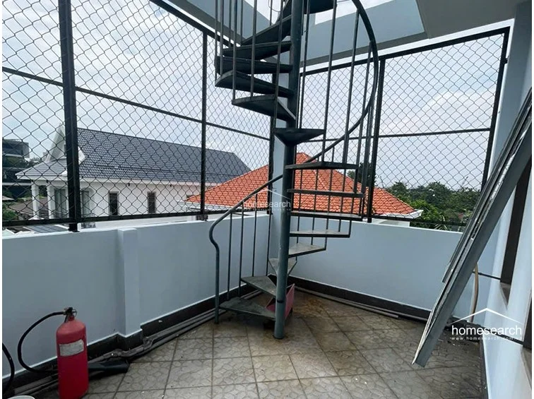 This outdoor terrace features durable patterned tile flooring and is fully enclosed with high metal safety fencing for security. A central spiral metal staircase provides unique access to different levels, and the space includes a fire extinguisher, suggesting a focus on safety and functional utility.