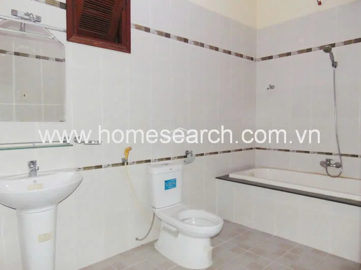 This bathroom features a functional layout with a pedestal sink, a standard toilet, and a combined shower-tub area. The walls are finished in white ceramic tiles with a decorative mosaic accent border, and the space includes a small wooden-framed vent window for ventilation.