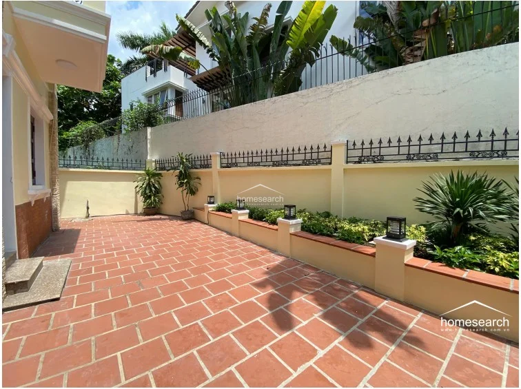 This outdoor garden area features durable terracotta tile flooring and raised planter beds filled with lush greenery. The space is enclosed by a high wall with decorative iron fencing, providing a private and secure environment for outdoor relaxation.