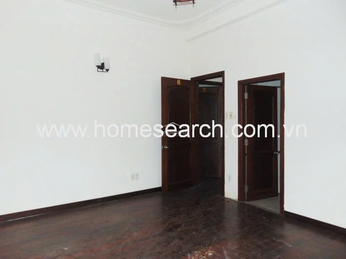 This interior room serves as a transition space, featuring dark hardwood flooring and multiple dark wood doors leading to other areas of the home. The walls are finished in a clean white, complemented by a simple wall-mounted light fixture and a minimalist, unfurnished layout.