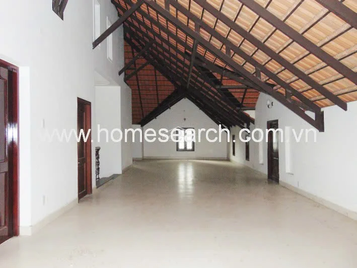 This expansive attic-style room is defined by its dramatic vaulted ceiling with exposed dark timber beams and terracotta roof tiles. The space is open-plan with smooth, light-colored flooring, white walls, and multiple entry points, offering a versatile area with significant architectural character.