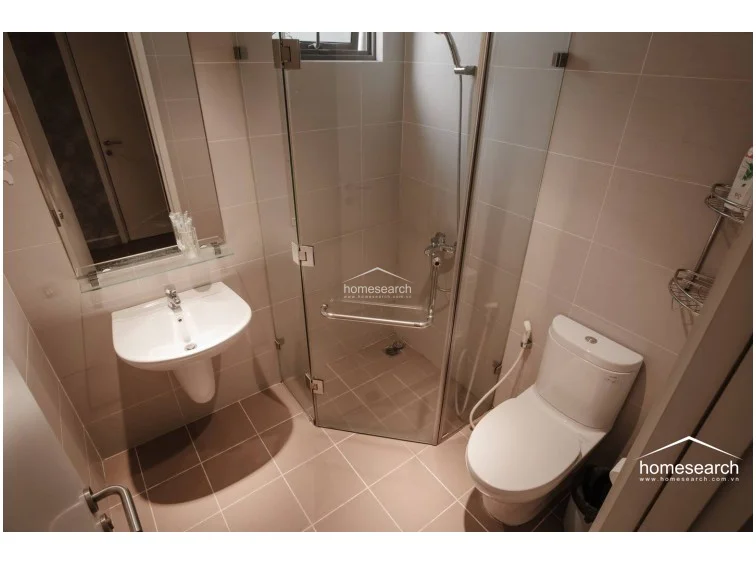 This view highlights the bathroom's practical configuration, including a handheld shower fixture and a convenient corner storage rack for toiletries. The space is well-lit with recessed lighting and maintains a cohesive, minimalist style throughout.