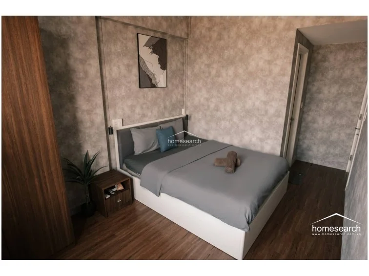 The layout is efficient, utilizing a recessed wall section to frame the bed, which helps maximize the limited floor area. The room is well-maintained and includes a wall-mounted air conditioning unit, ensuring comfort in this cozy, contemporary sleeping environment.