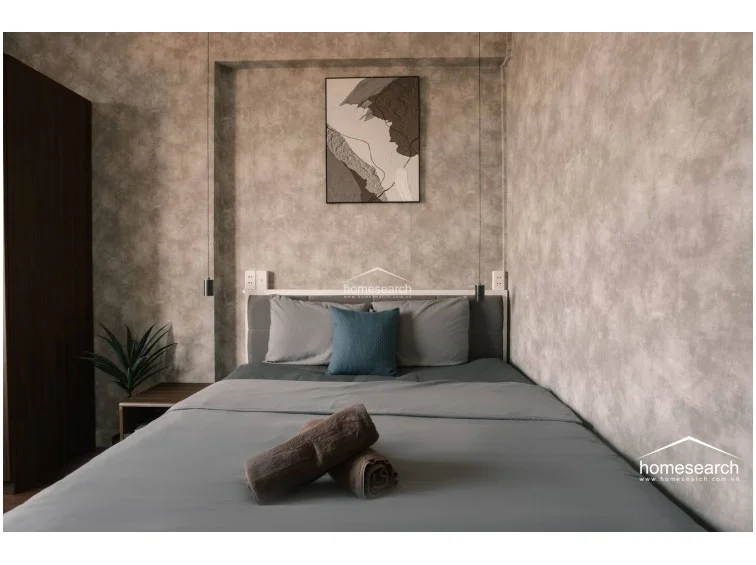 The bedroom utilizes a sophisticated, monochromatic color palette that emphasizes a clean, hotel-like atmosphere. The inclusion of decorative wall art and soft pendant lighting adds a touch of elegance to the functional, space-saving design.
