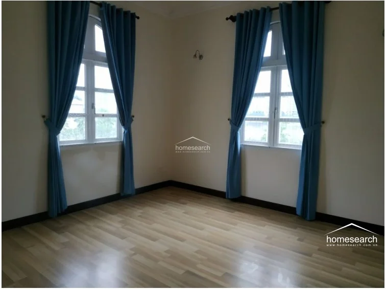 This bedroom features light-toned wood flooring and neutral walls, creating a clean and airy atmosphere. The space is equipped with a wall-mounted AC unit, a ceiling fan, and a glass-paneled door that opens to a balcony, allowing for natural light and outdoor access.
