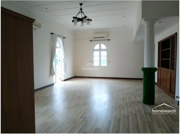 This bedroom maintains a consistent design language with dark hardwood floors, neutral walls, and a ceiling fan. It features a wall-mounted AC unit and a set of glass doors that provide direct access to an outdoor balcony area.