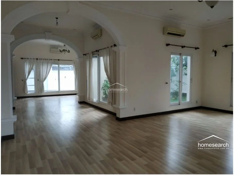 This bedroom features light wood-look flooring and cream-colored walls, creating a neutral and bright atmosphere. It is well-lit by two large arched windows dressed in blue curtains, and the space appears to be in good, clean condition.