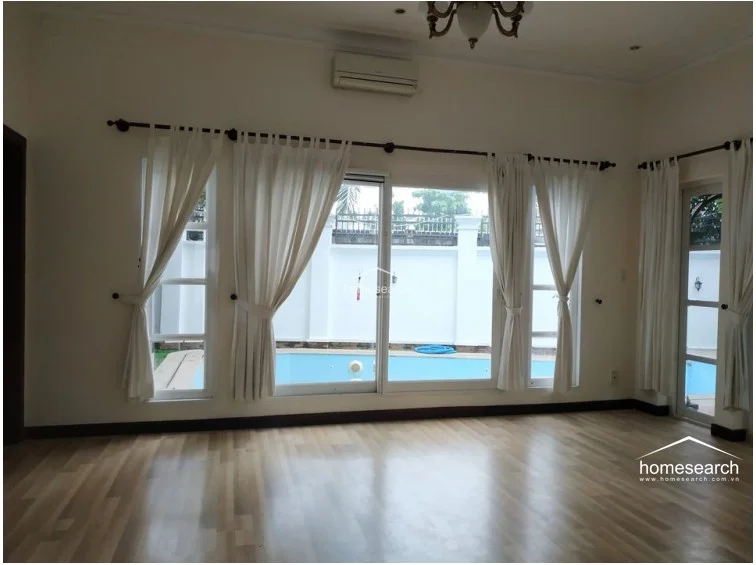 This room features a clean, versatile layout with a tray ceiling and recessed lighting, creating a refined architectural detail. The space is finished with light wood laminate flooring and large sliding windows that offer a view of the exterior, complemented by wall-mounted lighting fixtures. The room is in excellent condition, offering a bright and neutral canvas ready for furnishing.
