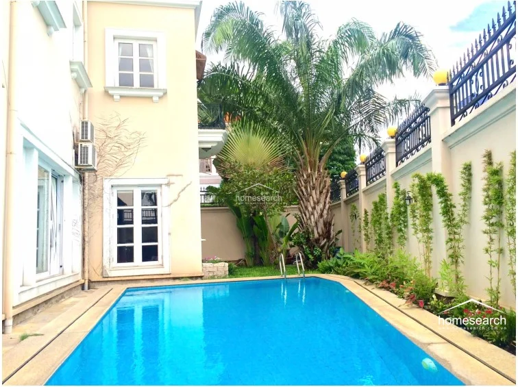 This image captures a lush side garden area featuring a mature palm tree and various tropical plants, providing a natural, shaded transition along the side of the house. The area is enclosed by a high, well-maintained perimeter wall, ensuring privacy and a tranquil environment.