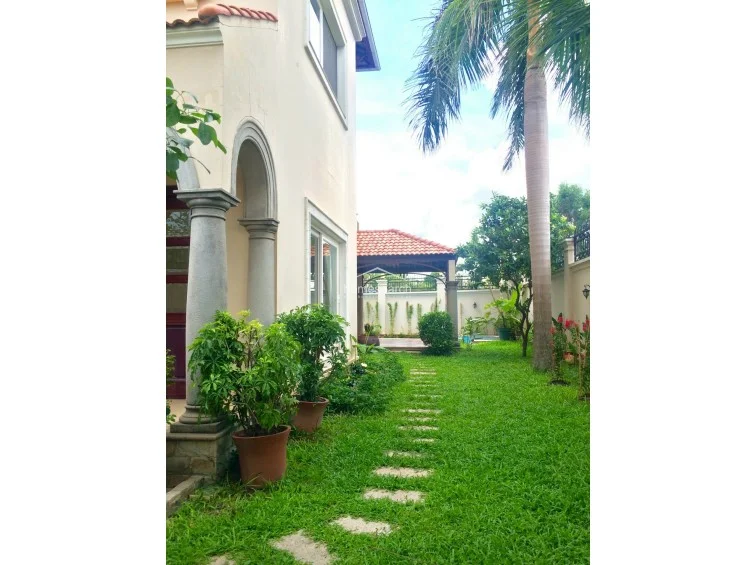 This view highlights the exterior side of the property, showing the pool’s edge and the transition from the tiled patio to a small patch of artificial turf. A wall-mounted AC unit is visible on the exterior wall, and the area is enclosed by a high white perimeter wall, providing privacy.