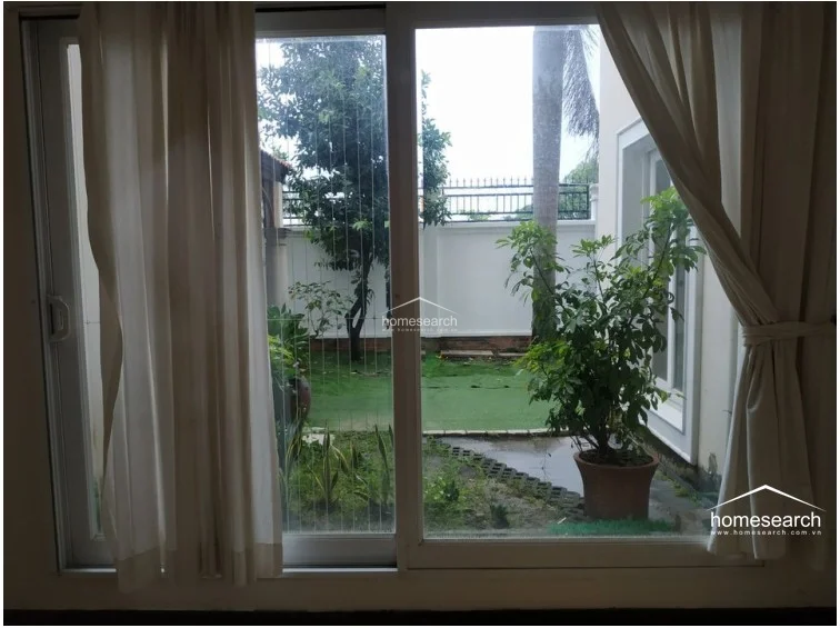 This view highlights the seamless flow of the ground floor, where large glass doors open directly onto an outdoor patio and garden space. The interior is characterized by high ceilings, decorative archways, and light wood flooring, creating a bright and airy environment. The space is well-maintained, featuring wall-mounted AC units and neutral curtains that enhance the home's sophisticated, open feel.