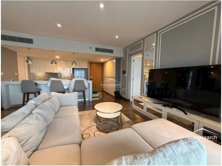 This open-concept living and dining area features a modern, neutral color palette with sophisticated wall molding and dark hardwood flooring. The space is anchored by a large, plush sectional sofa and a sleek kitchen island with bar seating, all illuminated by recessed lighting and stylish pendant fixtures.