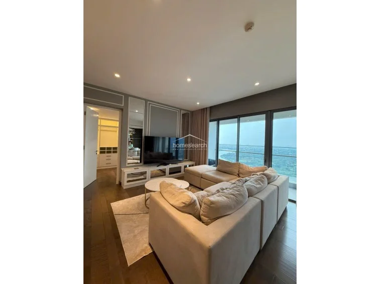 The living room is anchored by a large, comfortable modular sofa and a sleek media console, perfectly positioned for viewing. The sophisticated design includes recessed ceiling lighting and a seamless flow into the adjacent kitchen and dining area.