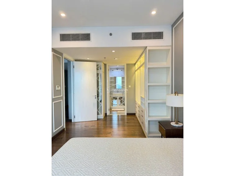 The bedroom features an integrated storage solution with open shelving and a dedicated walk-in closet area. The room maintains a cohesive aesthetic with wood flooring, recessed lighting, and a clear, functional flow leading directly into the en-suite bathroom.